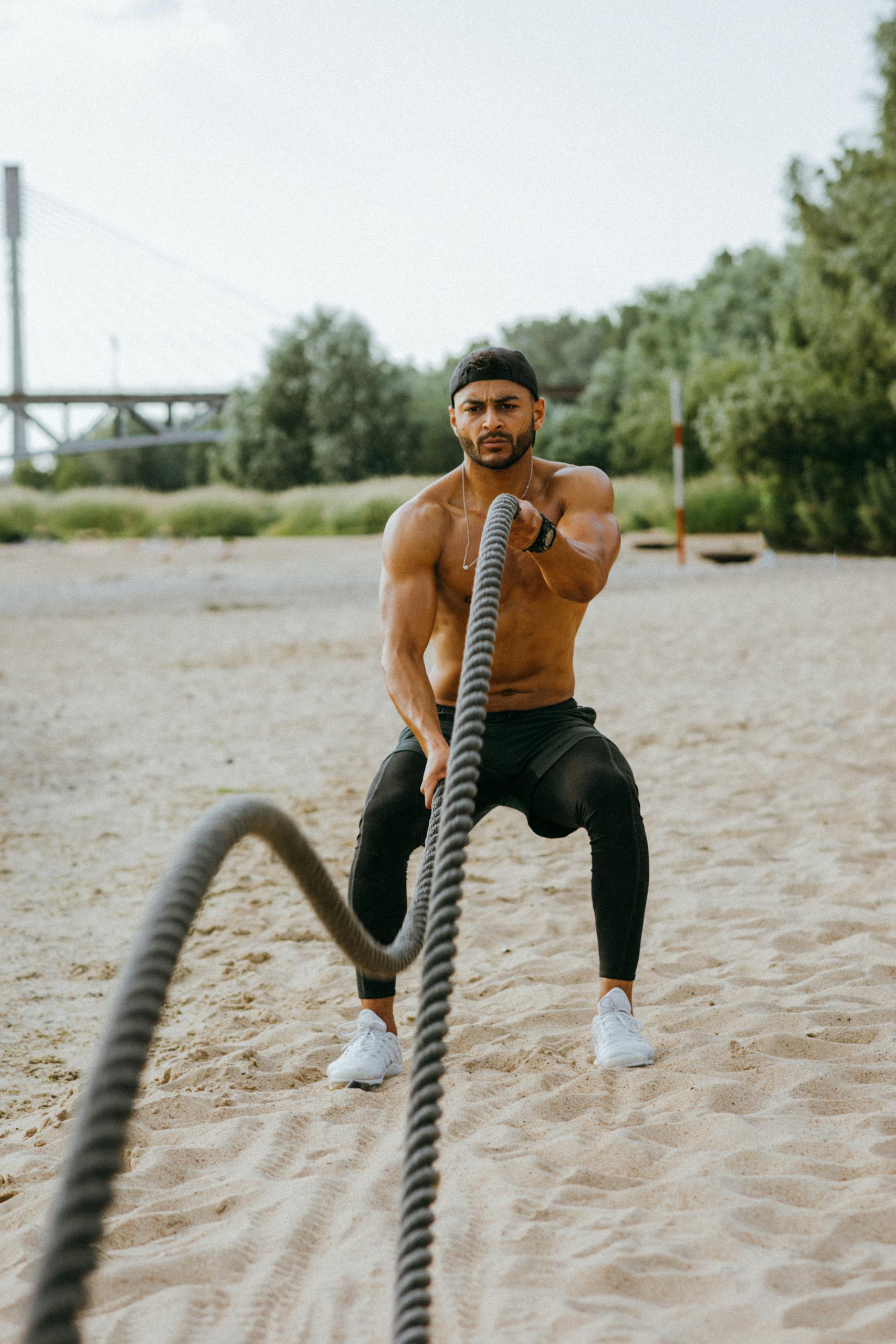 Fit man exercising with battle ropes on a sandy beach, showcasing strength and endurance.